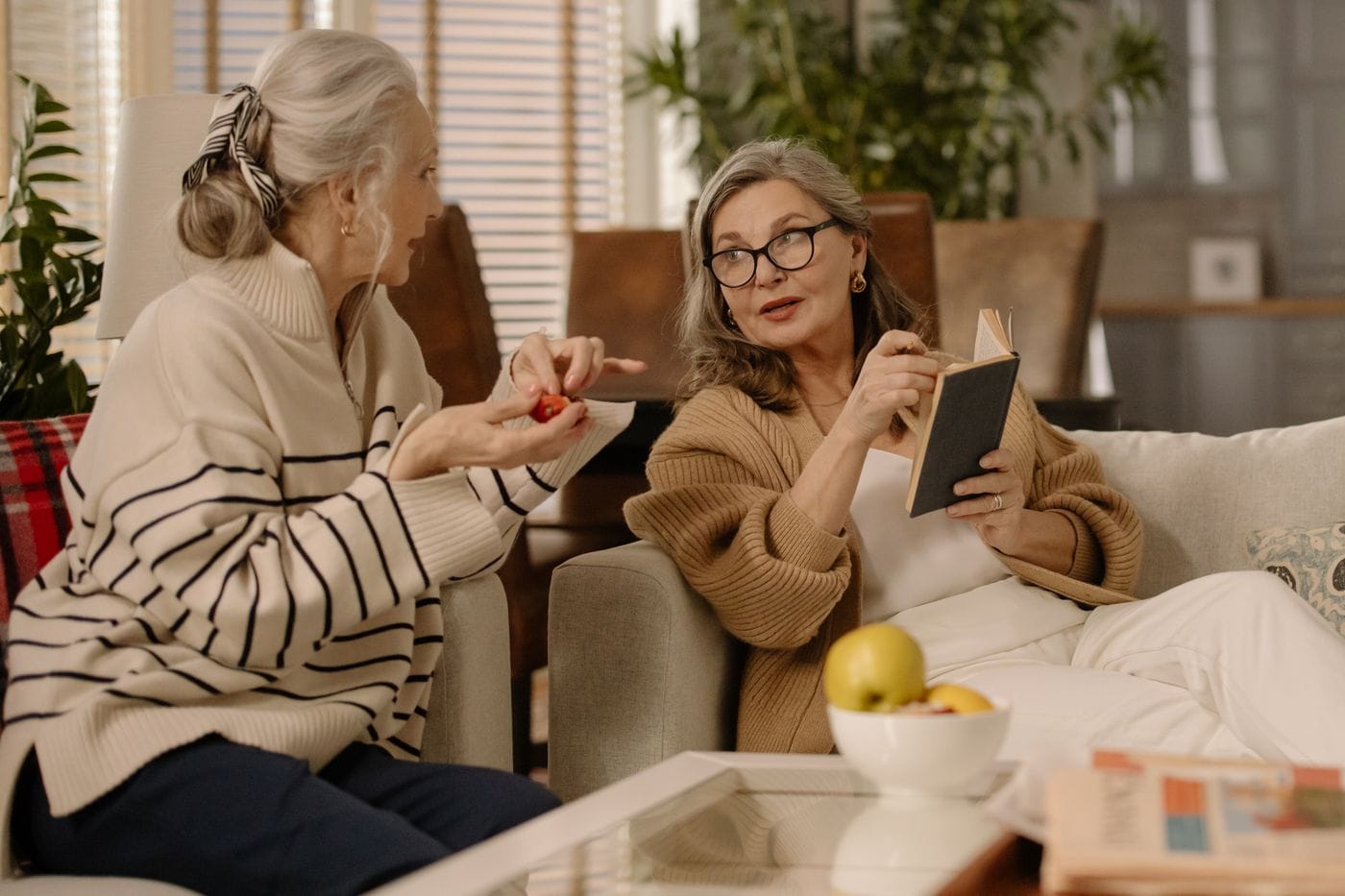Dos mujeres conversan sentadas en un sofá de tonos cálidos