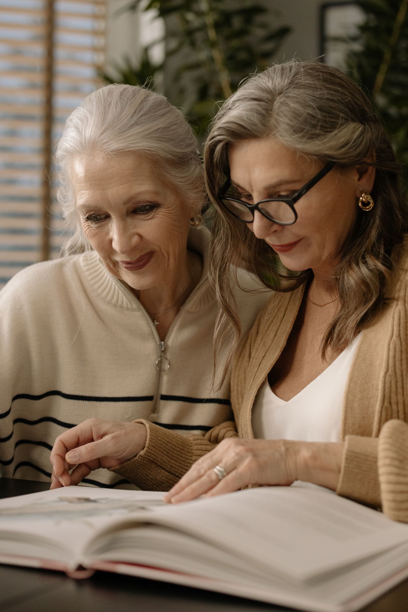 Dos mujeres comparten la lectura de un libro junto a una ventana